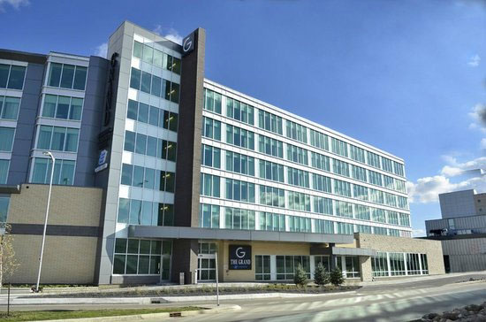The Grand, a multi-story hotel building with a glass facade and a prominent entrance sign under a clear blue sky.